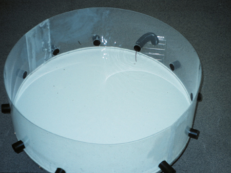 Vortex experiment setup, fluid dynamics; circular tank, transparent walls, flow observation.