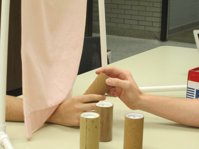 Psychology experiment with curtain setup; hand coordination task involving cylindrical objects.