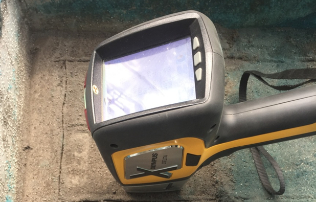 Handheld XRF analyzer scanning surface for elemental analysis; portable spectroscopy equipment.