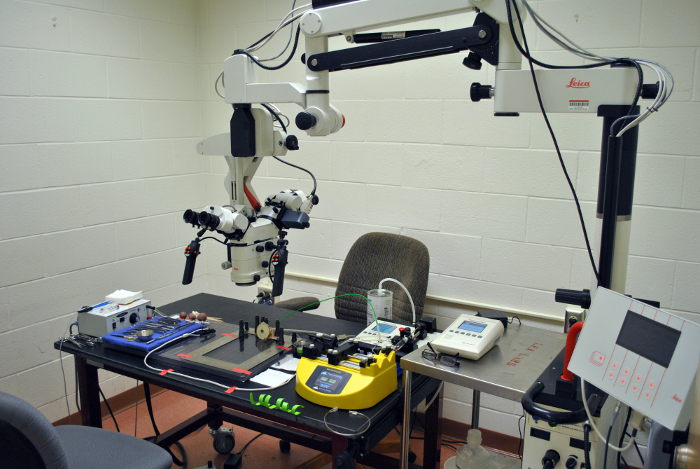 Configuração do microscópio cirúrgico para trabalhos de precisão; microscópio, painel de controle, ferramentas de bancada visíveis.