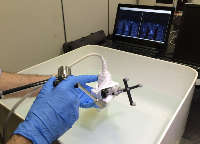 ultrasound imaging probe in water tank, laptop displaying results, non-destructive testing setup