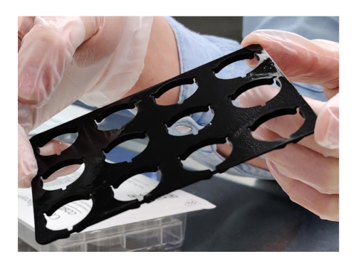 Lab equipment setup, material testing; gloved hands handling black sample holder, experimental analysis.
