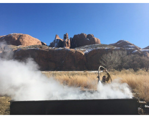 Outdoor boiling process; steam rising from outdoor container; natural setting; heat transfer concept.