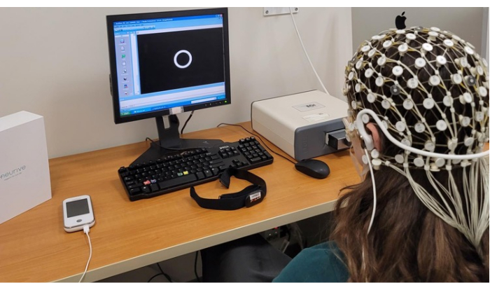 EEG brainwave analysis setup; participant with EEG cap monitoring cognitive responses on screen.