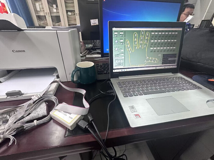 Hand biometric system, laptop screen shows fingerprint analysis software; setup on office desk.